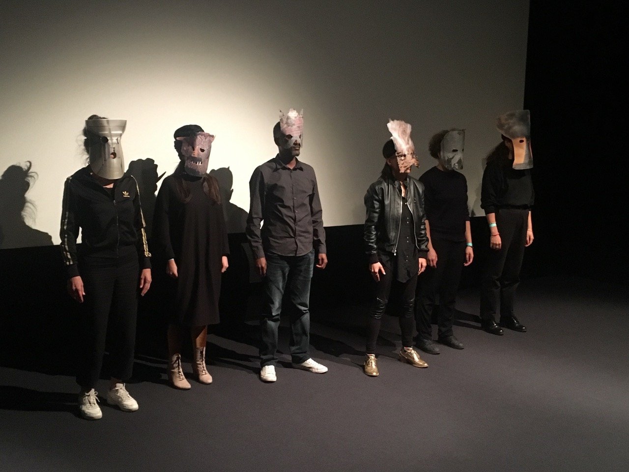 4 6 people in dark clothes with masks lined up in a row