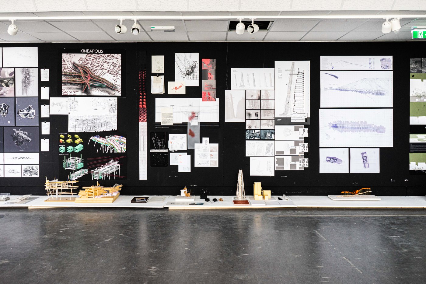 Finals, Design Studio ESC Bachelor, Foto ©Christina Maria Ehrmann, 2021 Auf einer schwarzen Wand hängen unterschiedliche Pläne, davor auf horizontalen Platten, stehen dazugehörige Architekturmodelle.