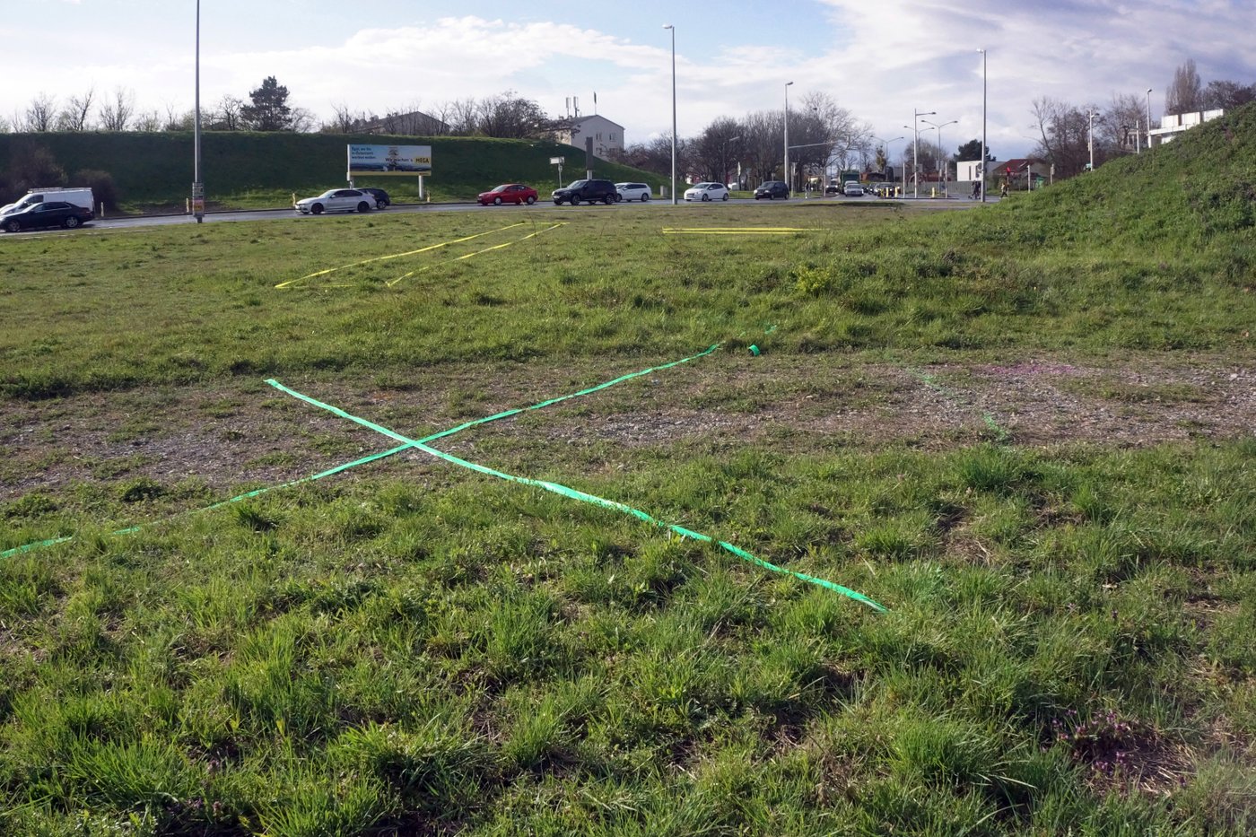 Verkehrsknoten, grüne und gelbe Markierungen in der Wiese mit Autos im Hintergrund