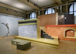 Ein Ausstellungsraum in einem alten Gebäude mit hohen Wänden und grossen bunten Ausstellungsstücken.