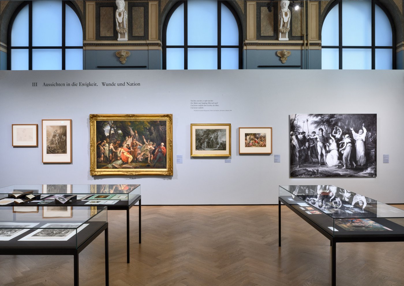 Ausstellungsraum mit unter anderem mit Gemälden an der Wand in Goldrahmen und Glasvitrinen