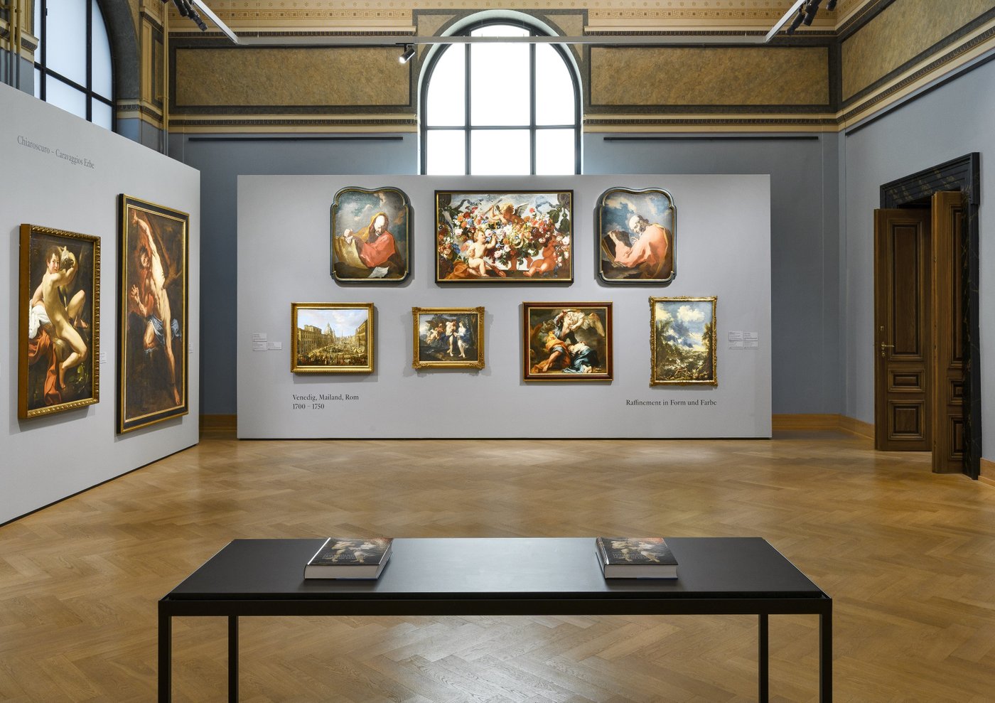 Ein blau ausgemalter Ausstellungsraum mit Gemälden an der Wand