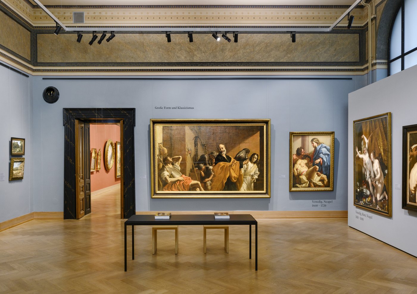 Ein blau ausgemalter Ausstellungsraum mit Gemälden an der Wand