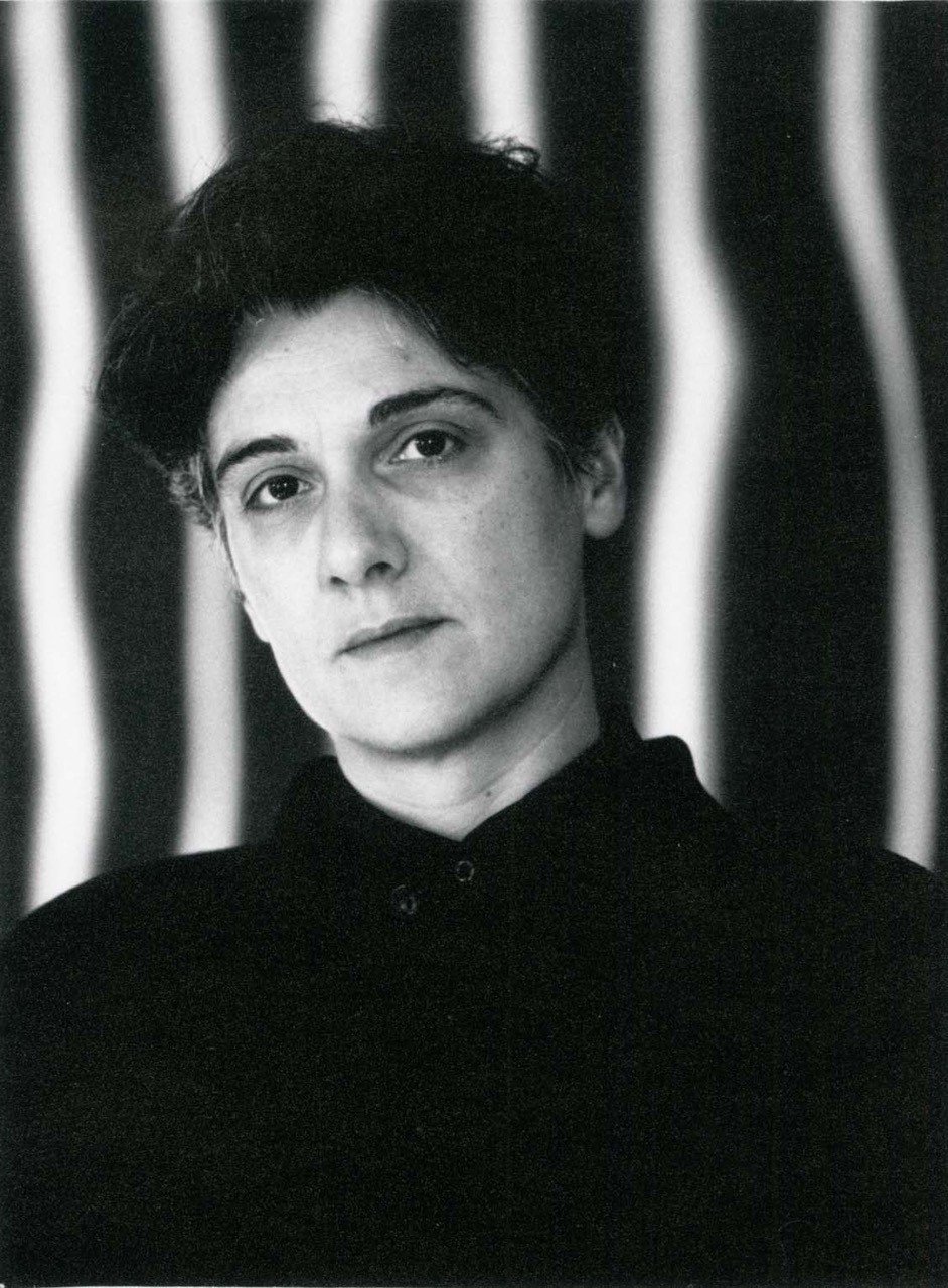 Nasrine Seraji, Foto A-125, UAAbKW Schwarz-Weiß-Foto von Prof. Nasrine Seraji, Porträtansicht von vorne mit kurzen dunklen Haaren, schwarzer Kleidung, vor gestreiftem Hintergrund.