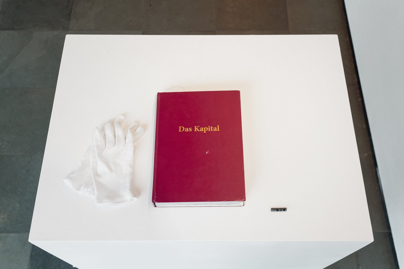 rotes Buch mit goldener Aufschrift liegt auf einem weißen Pult mit weißen Stoffhandschuhen daneben