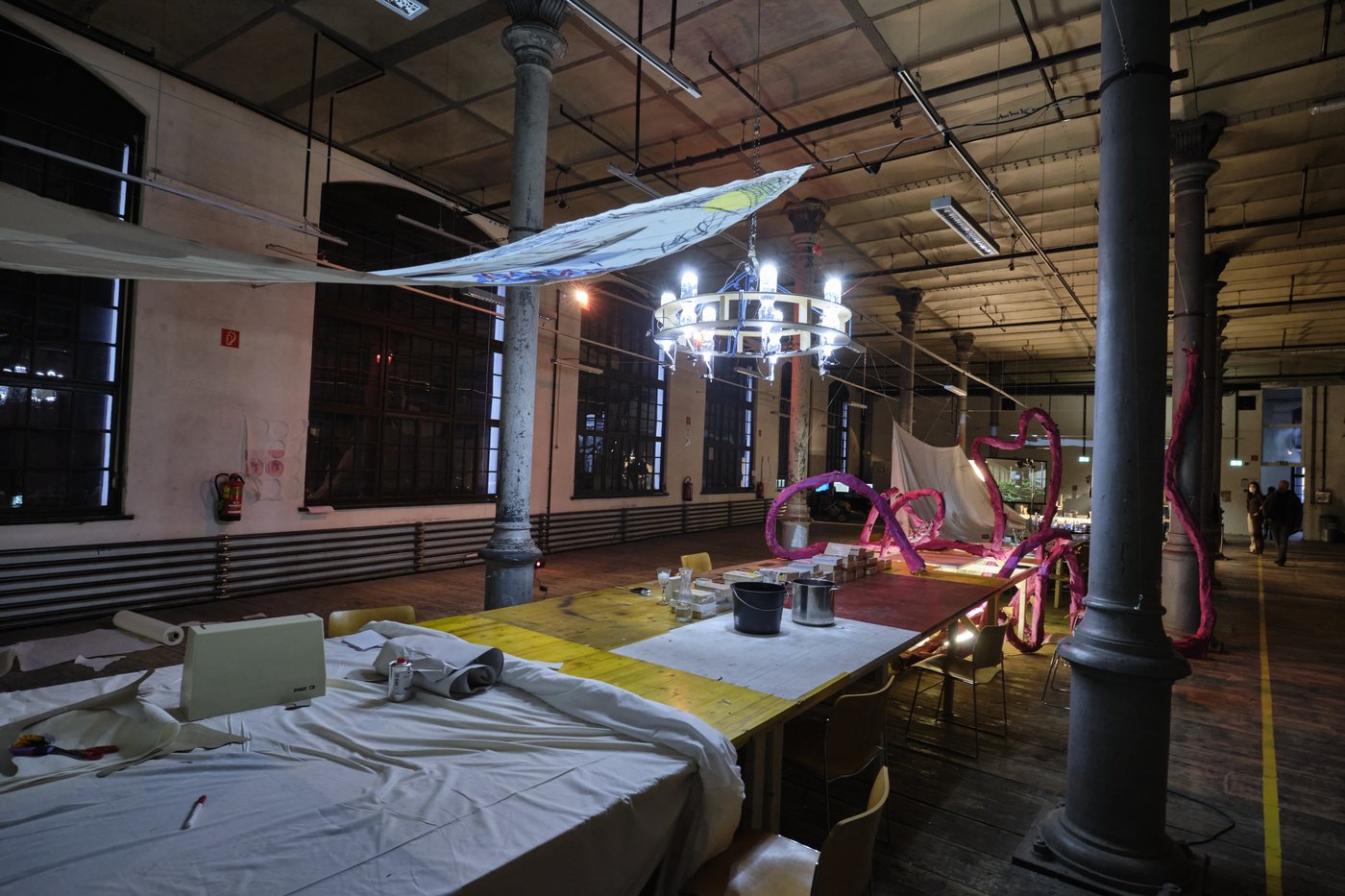 Spatial installation, Open Days 2022, photo © Lab_tf In the workroom of the stage design there is a long table with various working materials, a red paper snake, painted cloths stretched across the room above it and a chandelier.