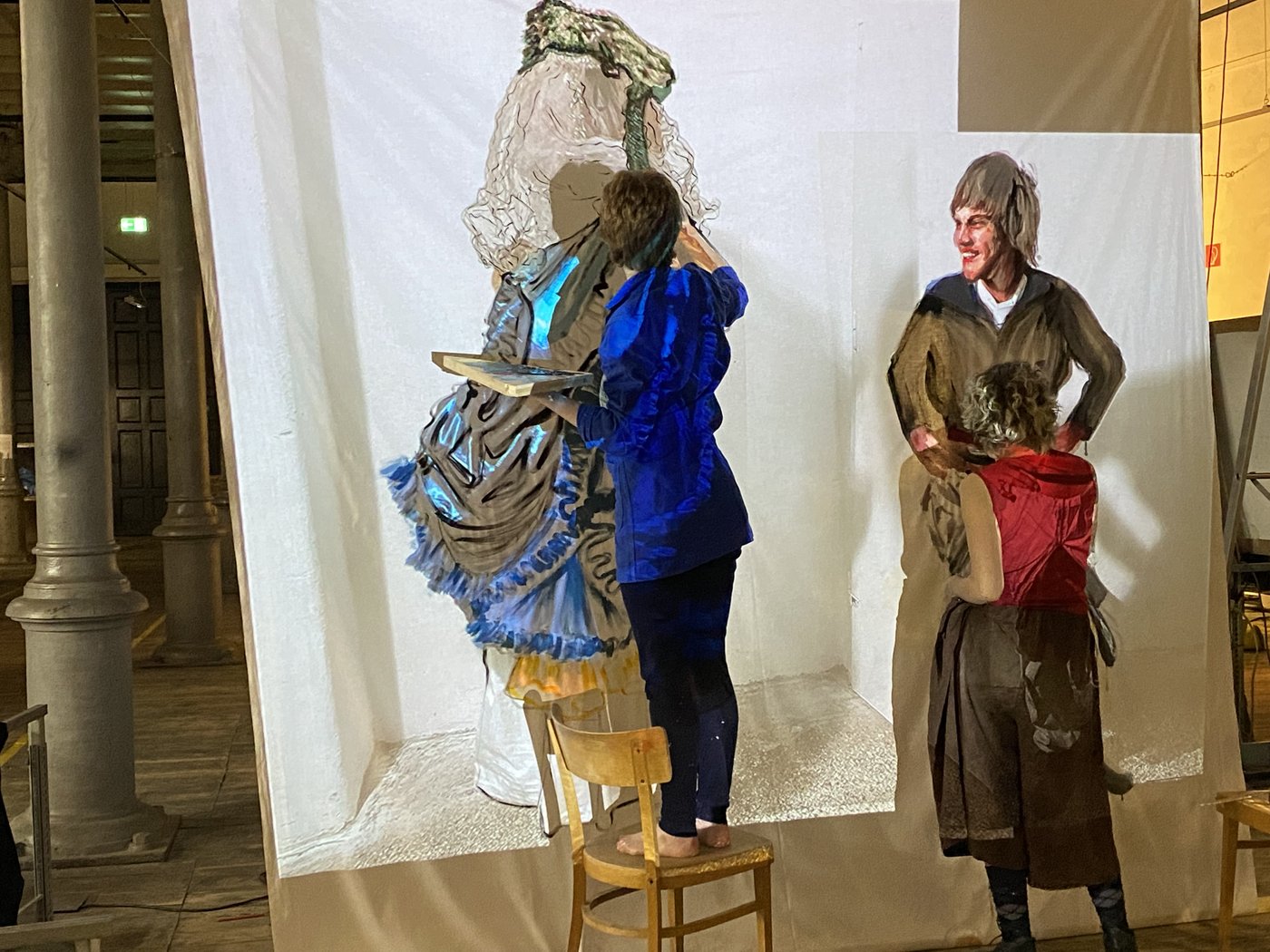 Costume Workshop, photo © Nina von Mechow Two students stand in front of a screen onto which costumes are projected and which they paint. One of them stands on a chair.
