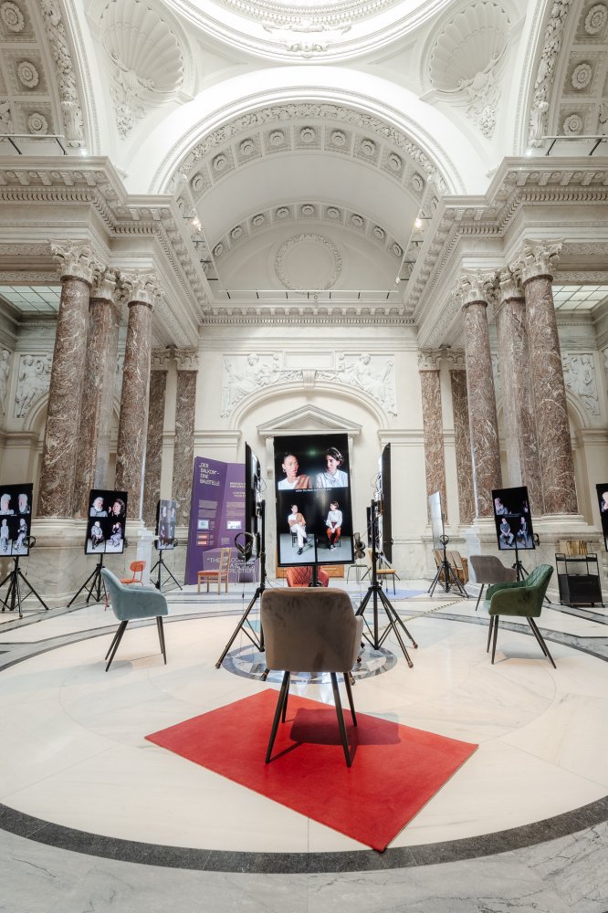 In a big open room with pillars are monitors with videos