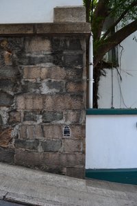 You can see a road or an asphalted path descending from left to right, a wall, a tree, a house wall.