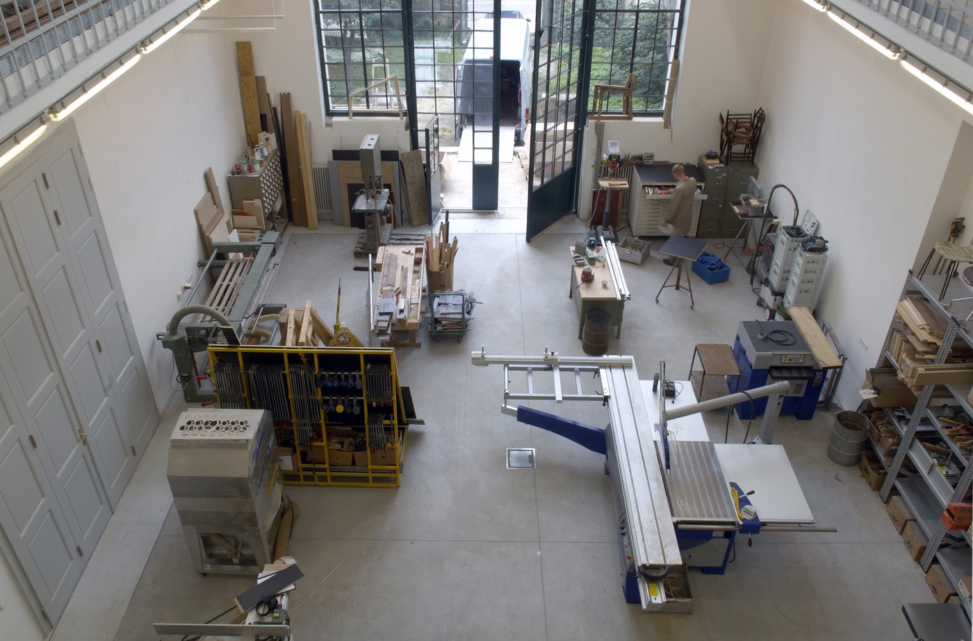 Wood workshop at Kurzbauergasse, photo © Lisa Rastl View into the workshop from above, you can see many tools for woodworking, shelves and wooden planks. In the background, the gate opens to the garden, where there is a van with an open loading area.